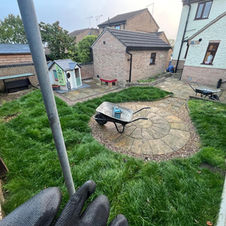 A clean backyard with large rectangular tiles, a curved grass section with mowing stripes, a black wooden fence with decorative stones, and a brick building with a diamond-patterned window