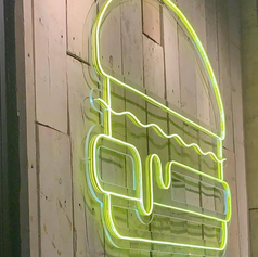 Minimalist green neon outline sign shaped like a hamburger on a wooden wall.