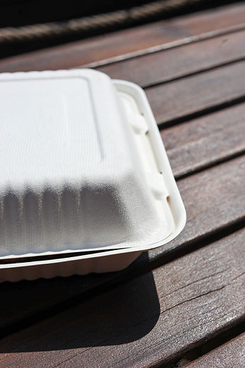 A closed, textured white compostable clamshell food container on an outdoor wooden table