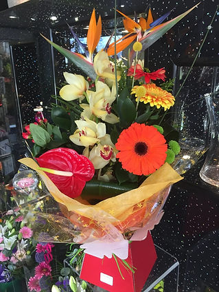 A vibrant bouquet featuring orange gerberas, yellow orchids, red anthuriums, and bird of paradise flowers