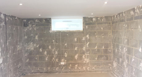 A dimly lit, unfinished basement with exposed concrete block walls, scattered plaster patches