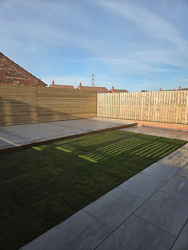 Artificial grass lawn with a grey block paved border and a brand new natural timber fence under a blue sky