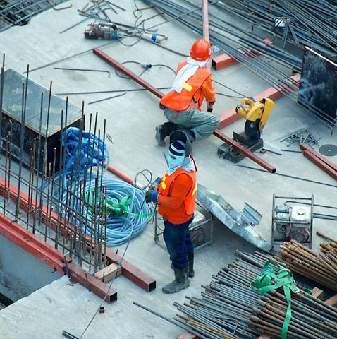 Two construction workers in orange safety vests and helmets work on a site
