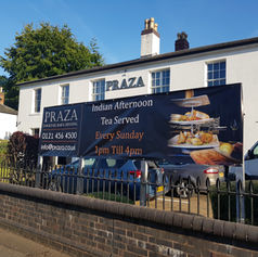 Large outdoor promotional banner fixed to railings in front of a white commercial building.