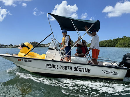 The Venice Youth Boating Association's support boat, adorned with a whimsical rubber ducky figurehead, is skillfully navigated by Beth Anderson of the Bitter Ends accompanied by crew member Chansi Harrow, Dinghy Dames and Bitter Ends volunteer Brian Acampa.