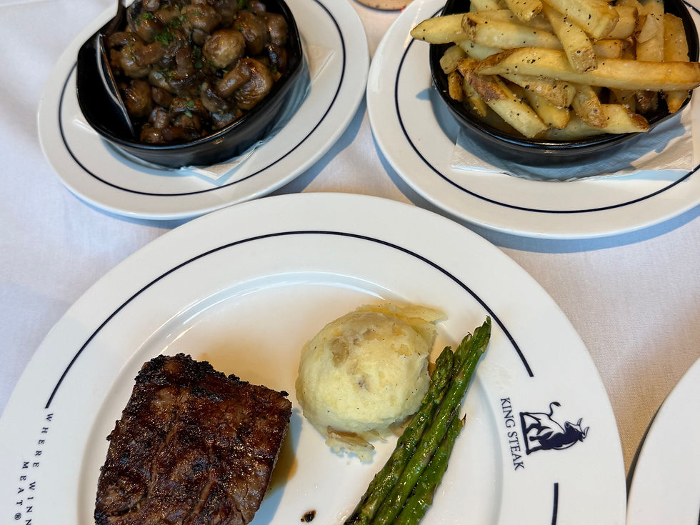 Steak, mashed potatoes, asparagus on a white plate labeled "King Steak", with sides of mushrooms and fries on a white tablecloth.