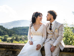 Mariés assis sur un muret en pierre face aux collines lors d'une séance photo de couple