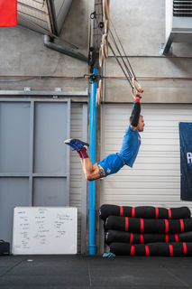 Homme musclé s'exerçant aux anneaux, soulevant son corps dans une salle de sport.