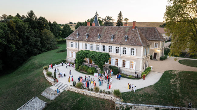 Grand château avec des invités, soirée festive, vue aérienne, ciel ensoleillé.
