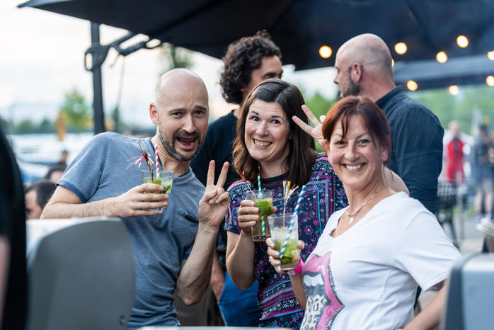 Groupe de personnes souriantes tenant des cocktails, montrant des signes de paix.