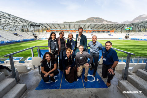 Groupe de personnes souriantes dans un stade face au terrain vert, Julien Barton