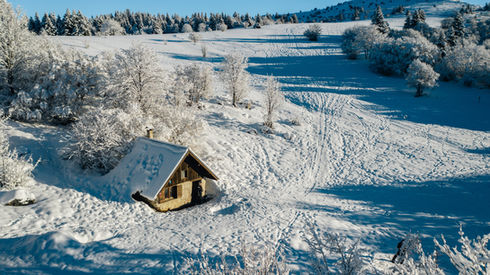Petite cabane enneigée, paysage hivernal ensoleillé avec arbres et collines, DRONE.