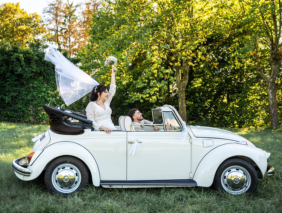Les mariés dans une Coccinelle cabriolet blanche, la mariée lève son bouquet et son voile