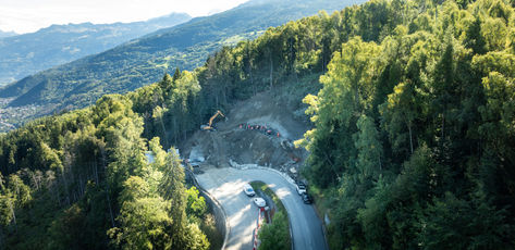 Vue aérienne d'une route en lacets bordée d'arbres et de montagnes.