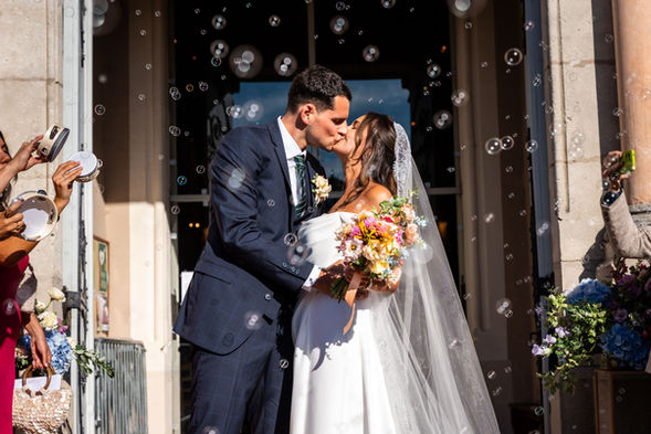 Couple s'embrassant devant une porte, bulles et bouquet, photographe vidéaste mariage