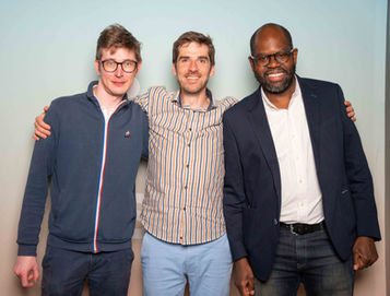 Trois hommes souriants posent ensemble; photo de groupe amicale et joyeuse.