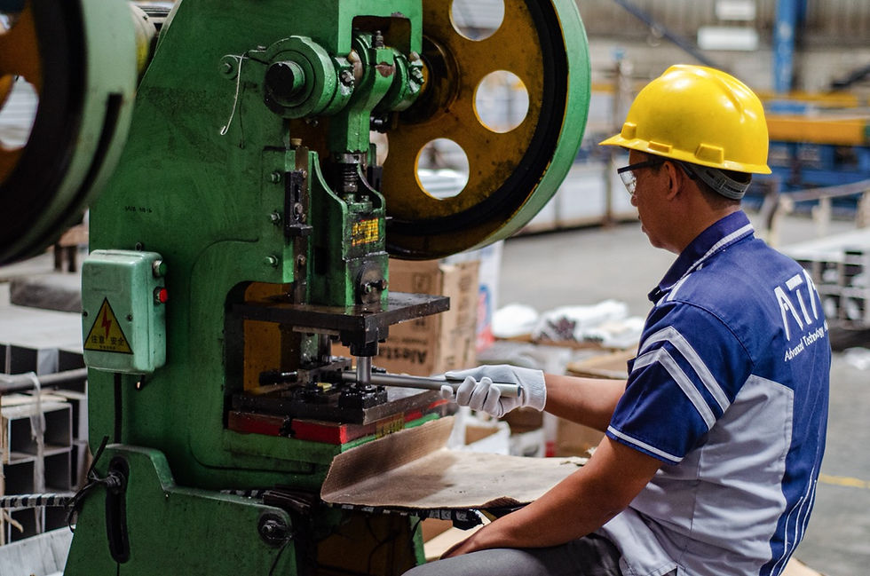 Man operates machinery in a factory setting with hard hat.