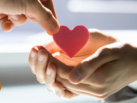 Hand giving a cutout red heart to another hand.