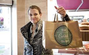 Female founder of To Good to Go Mette Lykke holding bag of food smiling in bakery.