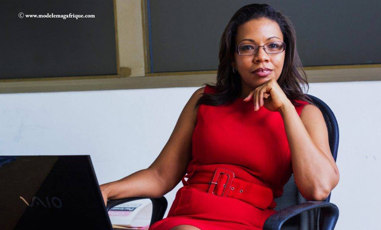 Tech businesswoman founder Rebecca Enonchong reclining in office chair with hand under chin in front of laptop in office.