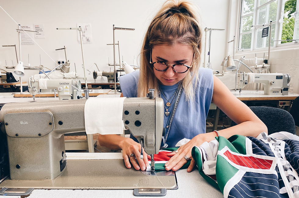 Woman sewing colorful fabric with a machine in a bright room. Focused expression, various sewing machines in the background, casual attire.