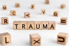 Wooden blocks spell "TRAUMA" against a white background, with additional scattered blocks showing random letters.