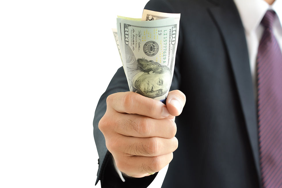 Businessman in a suit extends a hand holding U.S. dollar bills toward the viewer on a white background.