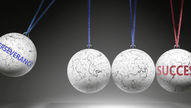 Four white spheres on strings, two with "PERSEVERANCE" and "SUCCESS" text. Marble texture, dark background. Suggests motion and focus.