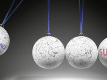 Four white spheres on strings, two with "PERSEVERANCE" and "SUCCESS" text. Marble texture, dark background. Suggests motion and focus.