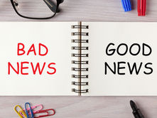 Open notebook on desk reads BAD NEWS in red and GOOD NEWS in black, with glasses, markers, paper clips, and a pen.