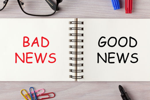 Open notebook on desk reads BAD NEWS in red and GOOD NEWS in black, with glasses, markers, paper clips, and a pen.