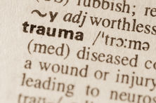 Close-up of the word "trauma" in bold in a dictionary. Surrounding text and phonetic spelling visible. Sepia-toned background.