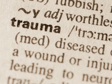 Close-up of the word "trauma" in bold in a dictionary. Surrounding text and phonetic spelling visible. Sepia-toned background.