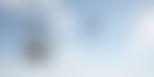 Bird flies away from an open hanging birdcage against a blue sky with clouds.