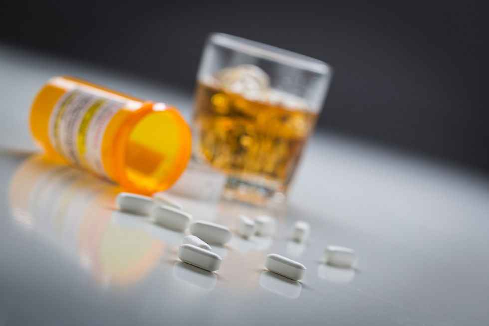 Spilled orange pill bottle with white tablets on a glossy table, beside a glass of whiskey, suggesting danger or misuse