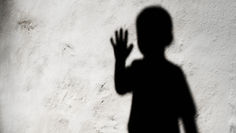 Shadow of a child with raised hand on a textured white wall, creating a mysterious and artistic mood.