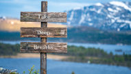 Rustic wooden sign with "Take Deep Breaths" text, set against a tranquil mountain and lake backdrop, evoking calmness and serenity.