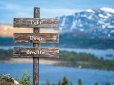 Rustic wooden sign with "Take Deep Breaths" text, set against a tranquil mountain and lake backdrop, evoking calmness and serenity.