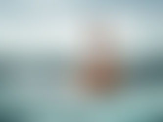 Man in a cardboard box paddles in the ocean, surrounded by shark fins. 