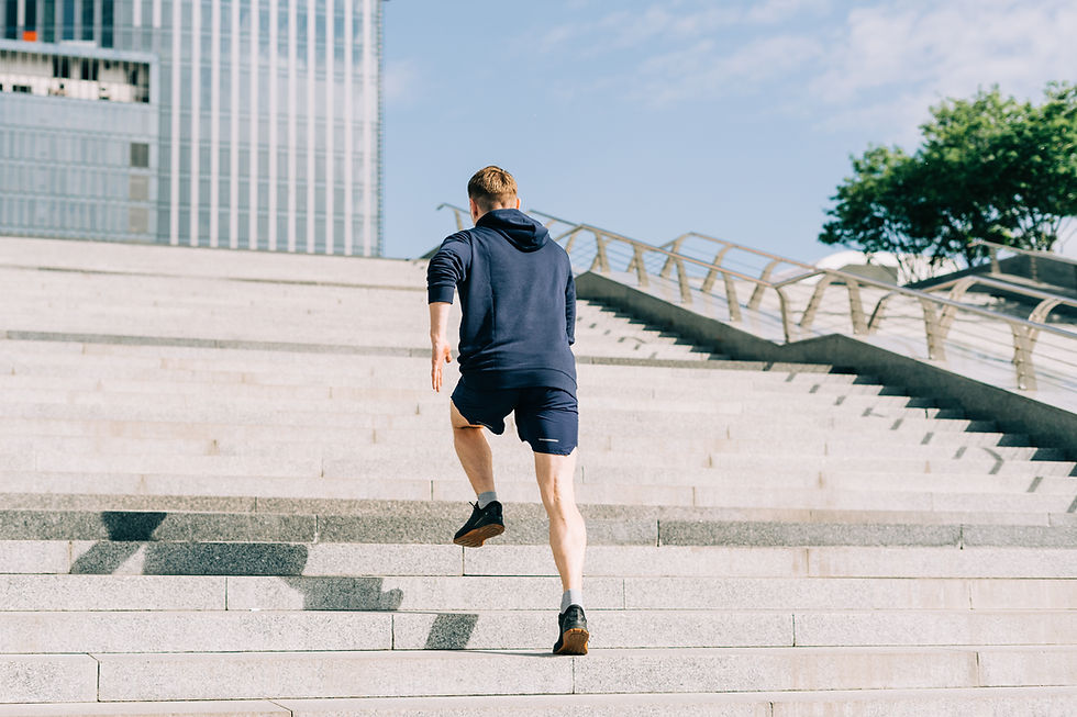 A man in navy athletic wear runs up a set of broad city steps beside a glass building under a bright blue sky.