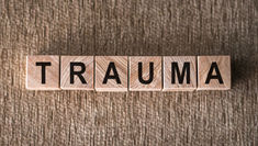 Wooden letter blocks spelling TRAUMA on a textured brown wood surface.