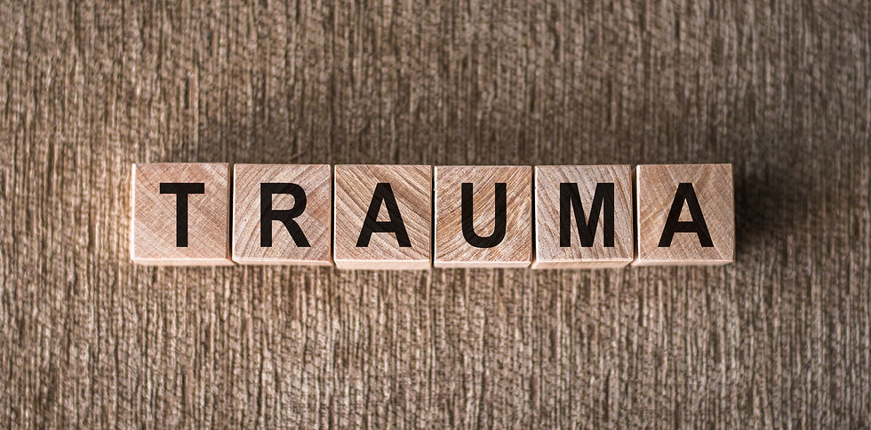 Wooden letter blocks spelling TRAUMA on a textured brown wood surface.