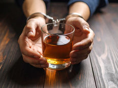 Hands in handcuffs hold a glass of amber liquid, highlighting the struggle against addiction.