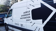 White mobile overdose prevention unit van parked on a city street, logos.