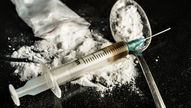 Syringe, spoon, and bag of white powder on a black surface, suggesting drug use.