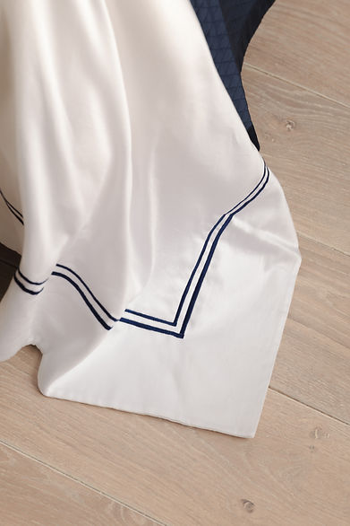 The corner of a duvet in sateen cotton with double cording in dark blue.