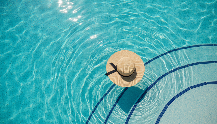 Overhead view of gentle ripples in a bright swimming pool with a sun hat floating near the edge.