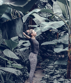 Woman with raised arms surrounded by lush green foliage Yomeja background