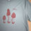 Thumbnail: Three morels printed in red on a light green grey shirt - Front detail