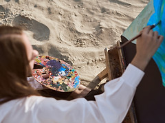 Young female artist paints on sandy beach, capturing vibrant colors of nature Serene seasi
